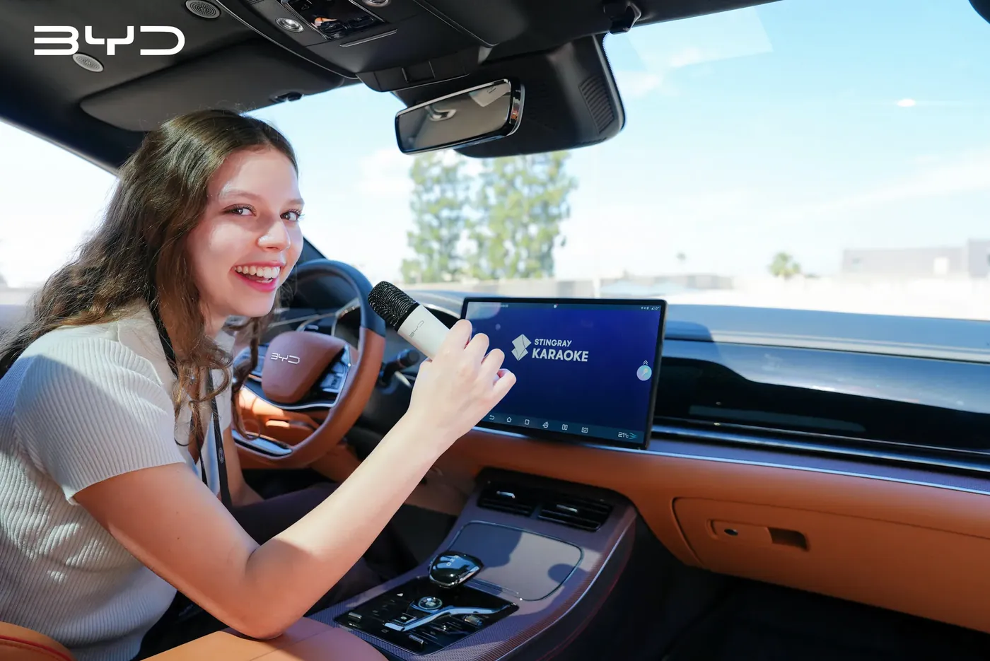 נוסעת ברכב BYD שרה עם מיקרופון מול אפליקציית Stingray Karaoke
